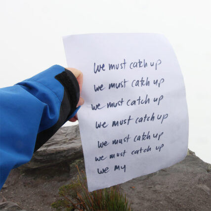 a hand holds a piece of paper at the top of a mountain