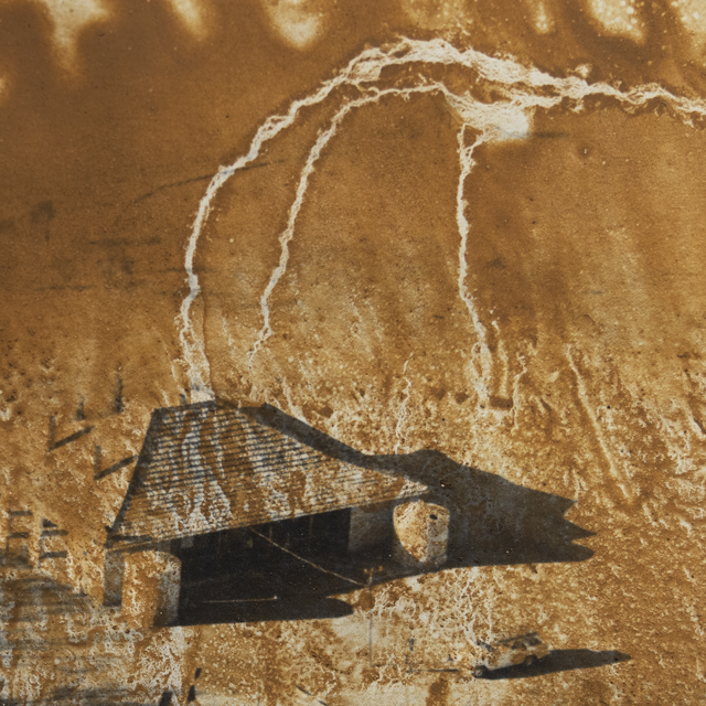 a black and white print of a house on an ochre-brown background. Water marks from the drying process make it look like lightning is hitting the house