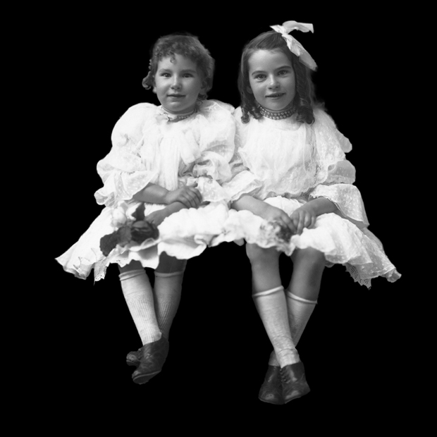 two girls dressed in old-fashioned white dresses cut out against a black background